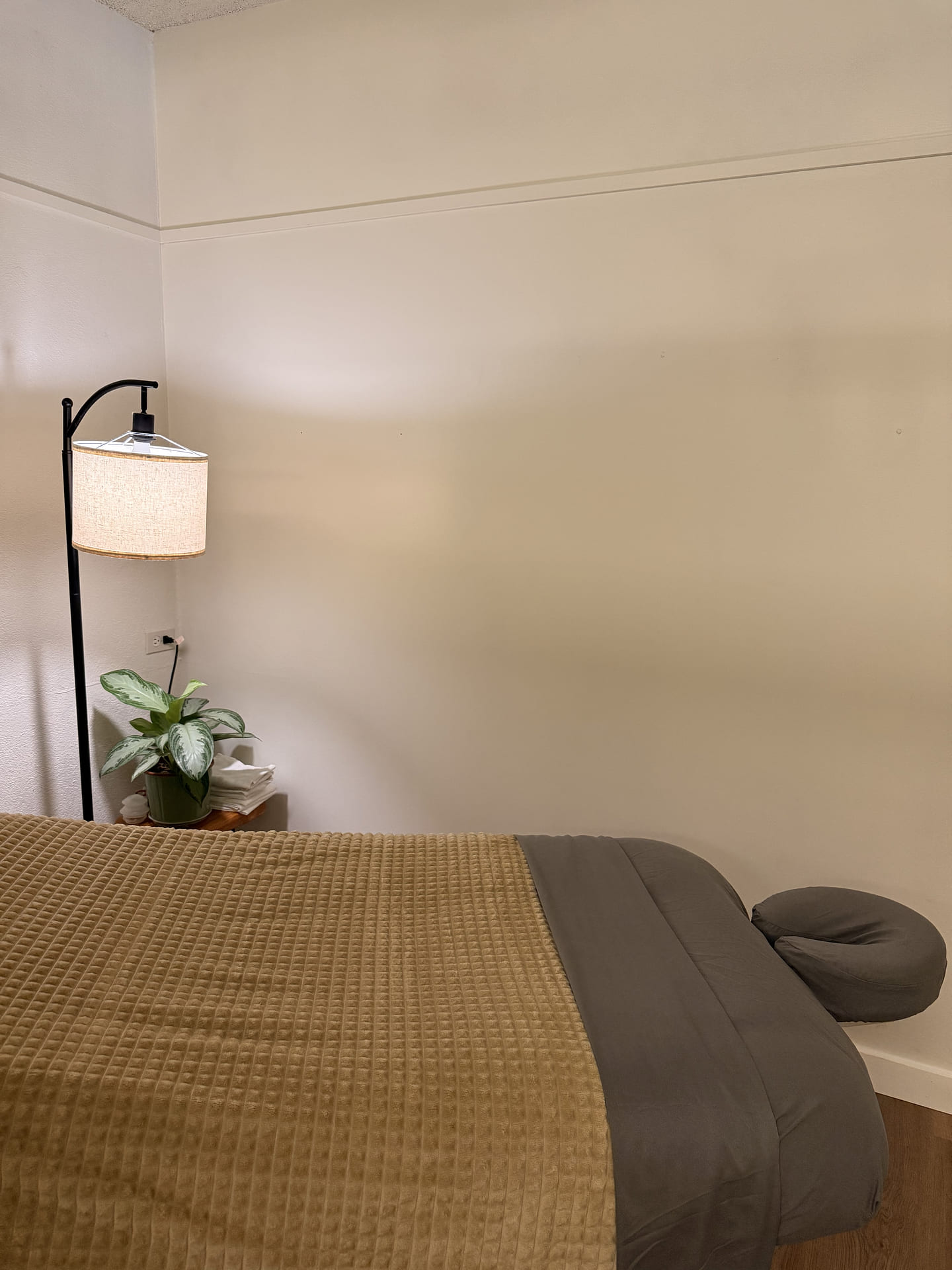 The massage table with a caramel blanket, a linen lamp and a plant beside it